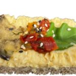 Bio-Vollkornbrötchen, bestrichen mit cremigem vegan Hummus, garniert mit Melansani und Paprika.