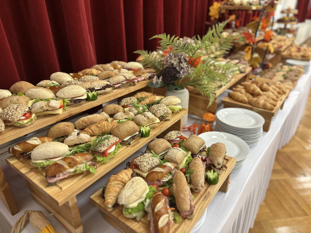 Fingerfood-Buffet mit vielfältigen belegten Weckerl, Laugengebäck und Croissants auf Holz­etageren, herbstlich dekoriert.